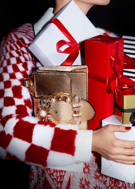 Woman wearing a fur checkered coat while holding wrapped Christmas presents and a gold bag with whit...