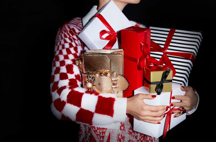Woman wearing a fur checkered coat while holding wrapped Christmas presents and a gold bag with whit...