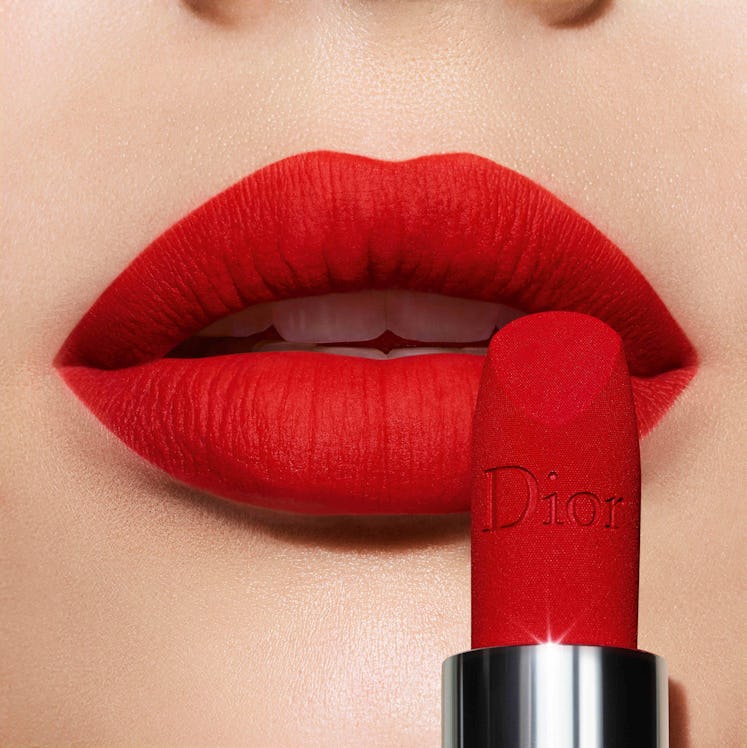A woman putting a red Dior lipstick on her lips