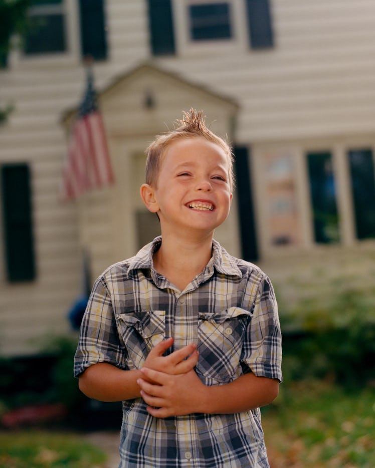 A smiling young boy in a blue-white checked shirt posing for Matthew So’s series, Picture Day 2020.