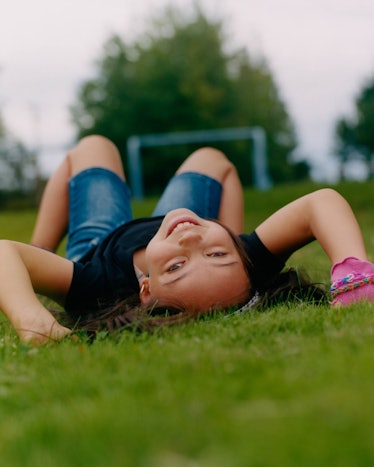 A little girl in a black shirt and blue denim shorts smiling posing for Matthew So’s series, Picture...