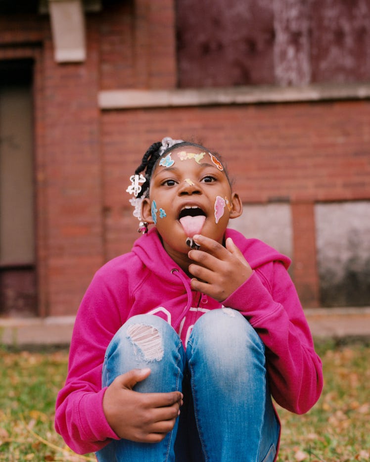 A little girl in a pink hoodie and blue denim jeans with face stickers posing for Matthew So’s serie...