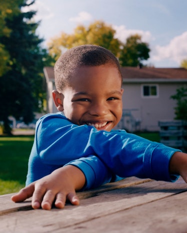A little boy in a blue shirt smiling with his arms crossed and posing for Matthew So’s series, Pictu...