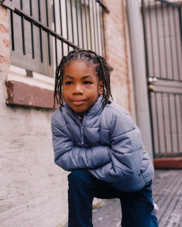 A boy in a grey puffer jacket and blue denim pants posing for Matthew So’s series, Picture Day 2020.