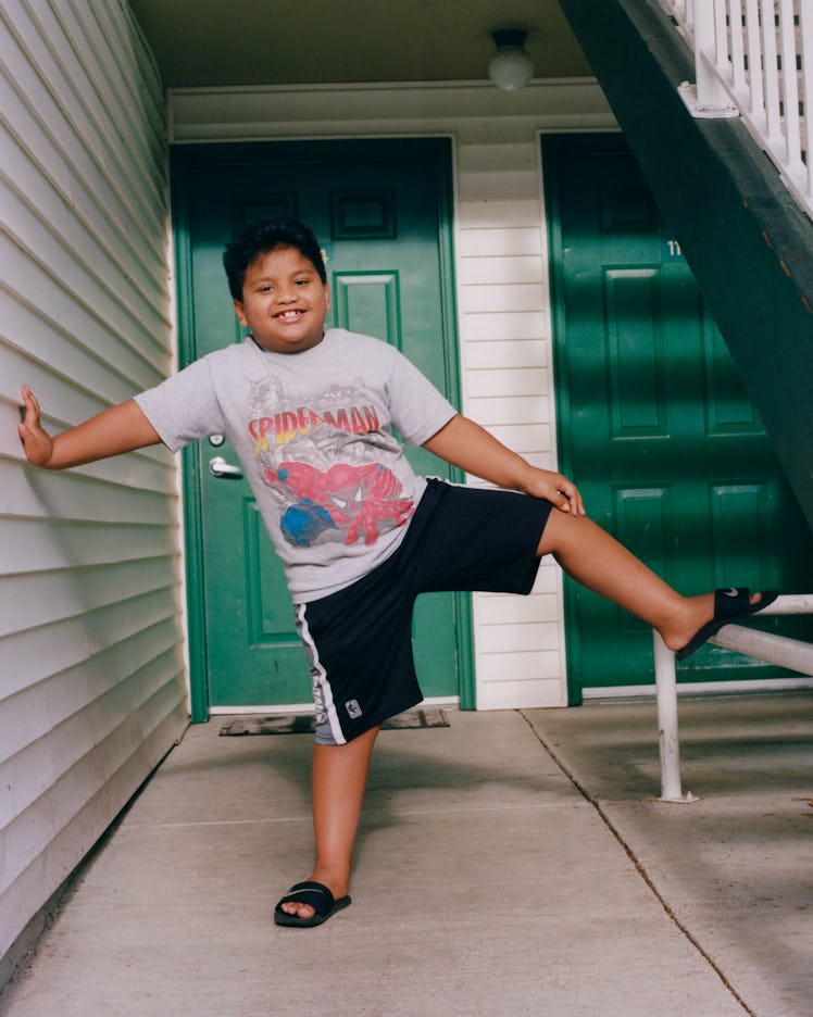 A boy in a grey Spider-Man shirt and black shorts smiling and posing for Matthew So’s series, Pictur...