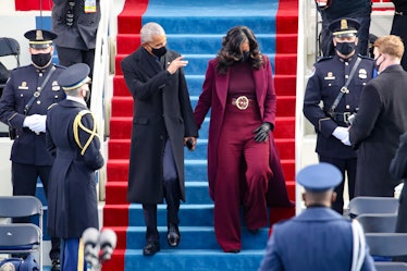 Barack Obama in a black suit and coat and Michelle Obama in a burgundy coat, trousers and sweater
