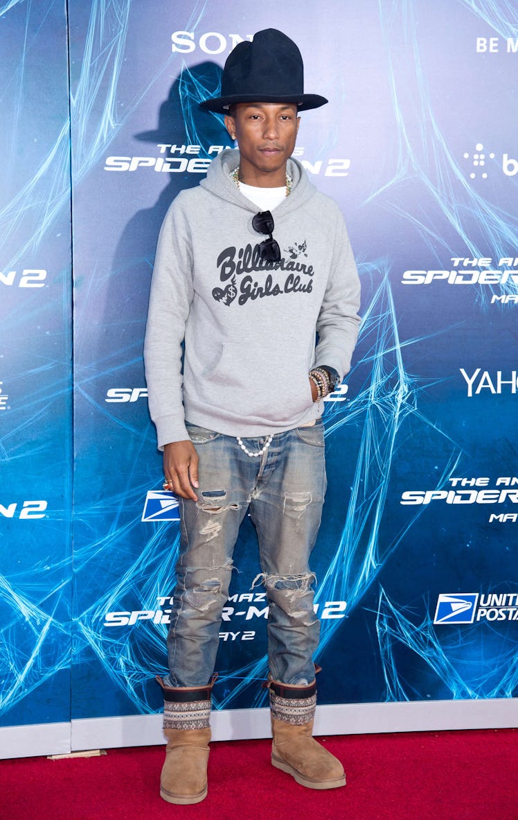 Pharrell Williams posing on a red carpet while wearing a hoodie, jeans, and Ugg boots