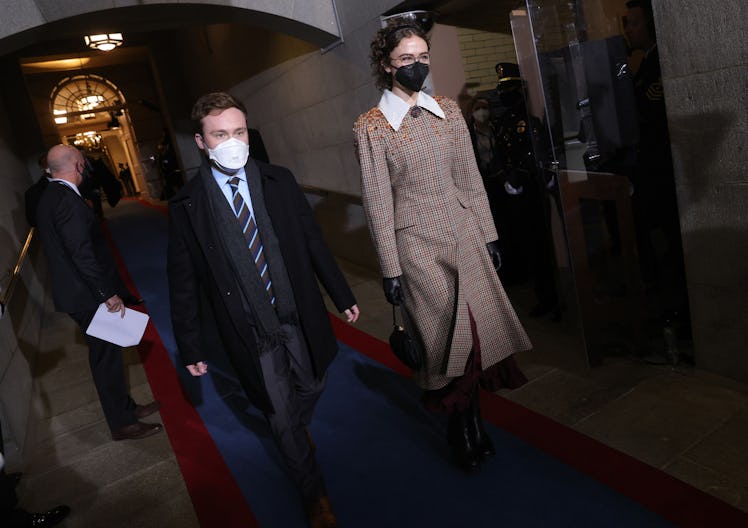 Cole Emhoff in a black suit and coat and Ella Emhoff in a beige coat walking down a hallway