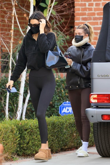 Kendall Jenner wearing short brown Ugg boots while Hailey Bieber is wearing white furry slippers whi...