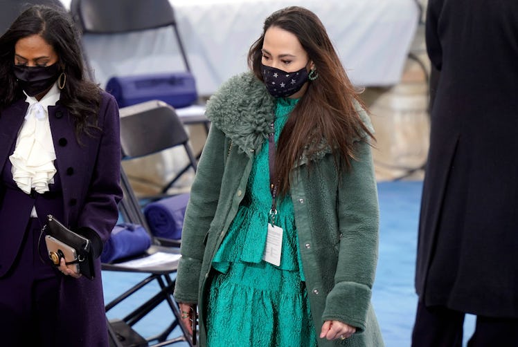 Meena Harris in a green dress and a green coat, and a black face mask walking