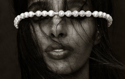 A model with messy dark hair over her hair and a pearl necklace by Wilfredo Rosado on her forehead