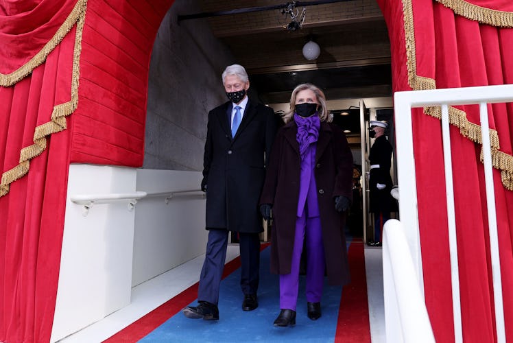 Bill Clinton in a navy suit and a black coat and Hillary Clinton in a purple suit and a black coat