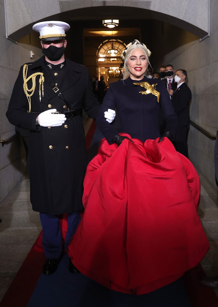 Lady Gaga in a black-red Schiaparelli dress with a golden bird, escorted by a man in a black uniform