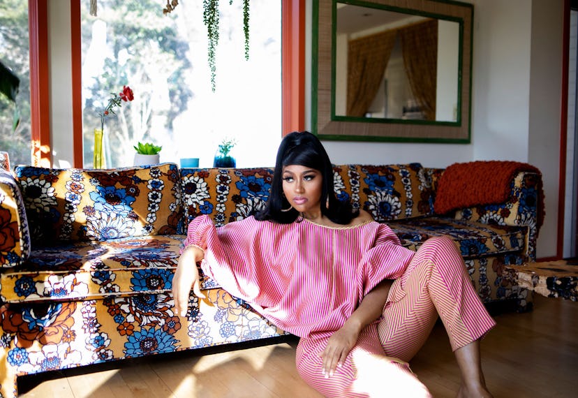Jazmine Sullivan on the floor, leaning against a couch in a striped pink loungewear set