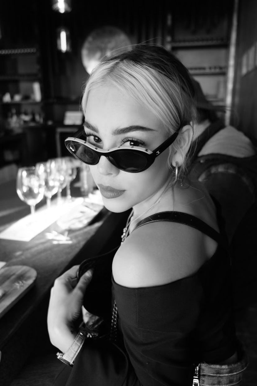 A black and white photo of Danna Paola looking to the camera, with her sunglasses on her nose 