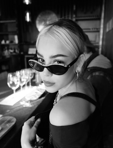 A black and white photo of Danna Paola looking to the camera, with her sunglasses on her nose 