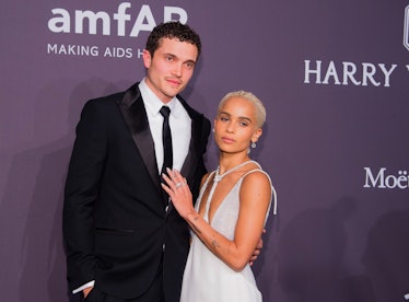 Karl Glusman in a black suit, a white shirt and a black tie and Zoe Kravitz in a white dress
