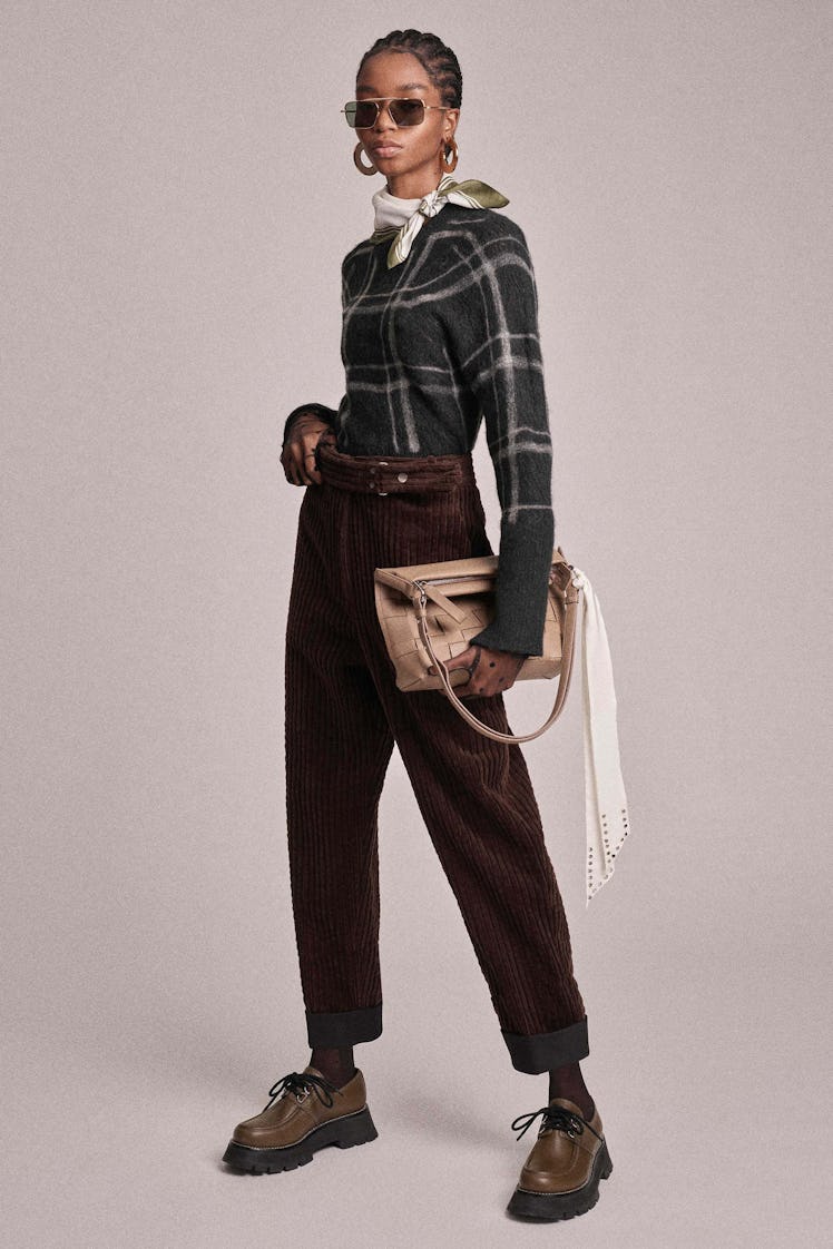 A model in a black plaid sweater and high-waisted pants with a beige bag by Phillip Lim