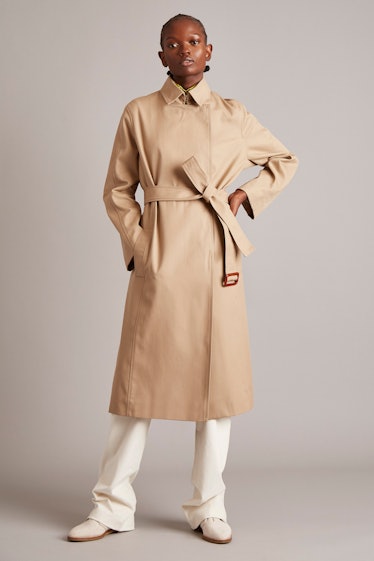 A model in a beige trench coat and white pants by Adam Lippes