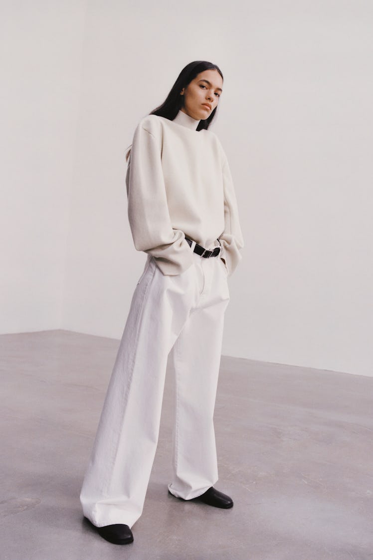 A model in a white sweater and wide-leg white pants by The Row 