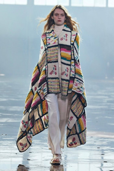 A model in white pants, a white sweater and a multipatterned poncho during NYFW by Gabriela Hearst