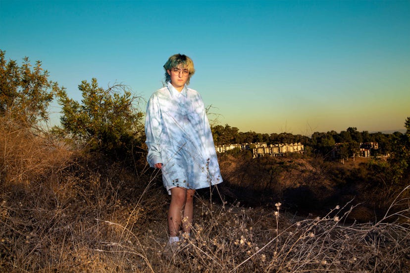 Claud Mintz posing in a field in an oversized tie-dye collared shirt