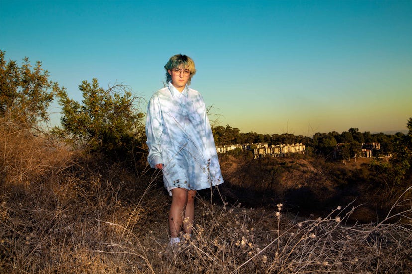 Claud Mintz posing in a field in an oversized tie-dye collared shirt 