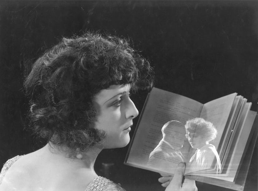 Lya De Putti looking at a book with a see-through image of a man and a woman hugging