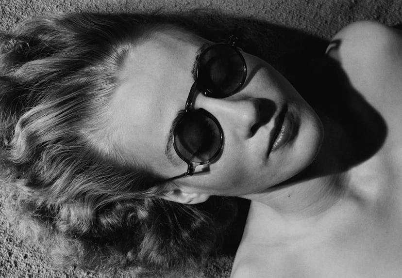 A woman lying on the sand with sunglasses having a hangover in a black-white image
