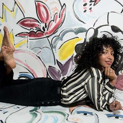 Nadeesha Godamunne posing on the floor in a sheer striped blouse and black pants 