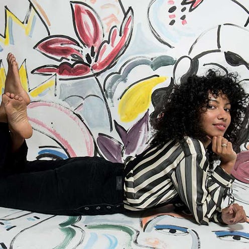 Nadeesha Godamunne posing on the floor in a sheer striped blouse and black pants