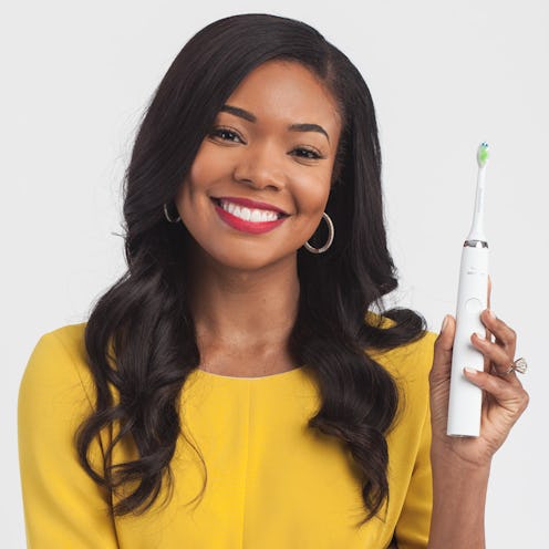 Gabrielle Union in a yellow top, smiling and holding up the Philips Sonicare toothbrush