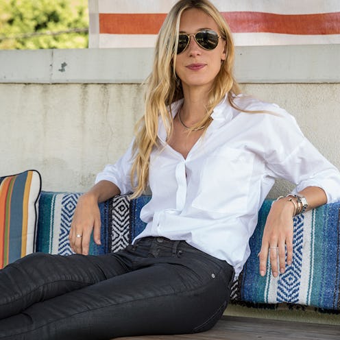 A blonde woman in a white button-up, black jeans and black sunglasses with her hair down