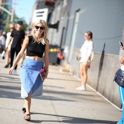 A woman walking down the street during Spring in a cropped black tank top and a blue skirt