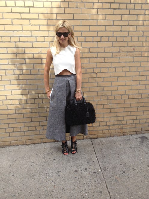 A blonde woman wearing neutral staples, a white top, and a grey skirt
