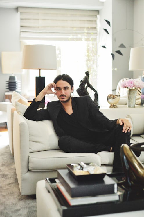 A man in a black suit sitting on a white couch in a glamourous home