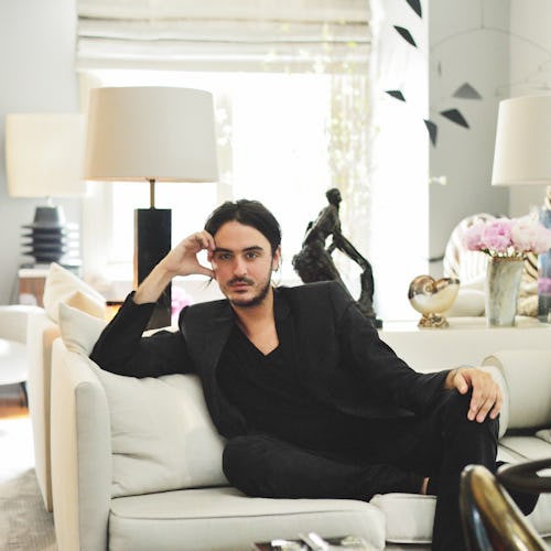 A man in a black suit sitting on a white couch in a glamourous home