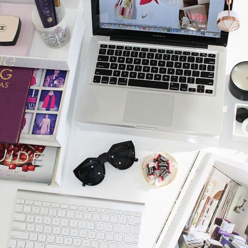 A desk in office with a laptop, keyboard, and sunglasses