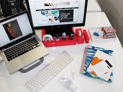 An office desk with a monitor, keyboard, laptop, and notebooks