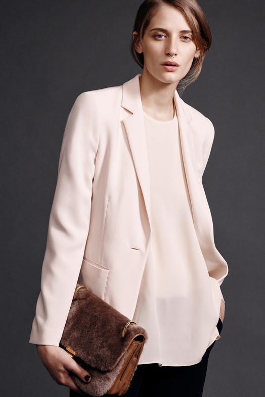 A model wearing a blouse and blazer in champagne holding Elizabeth & James' Teddy bear purse