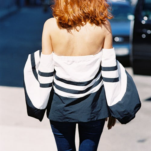 A woman with red hair walks away from the camera wearing a blue and white jacket that leaves her sho...
