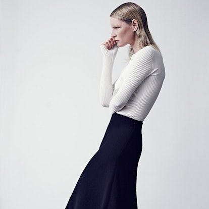 A model posing in Protagonist's white cashmere sweater and a black skirt