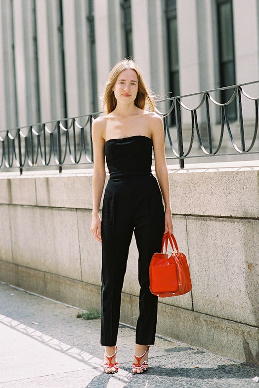 A young model posing in a black jumpsuit while holding a red bag 