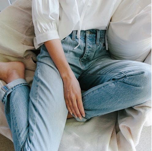A model sitting and posing in blue denim jeans and a white shirt by J.Crew