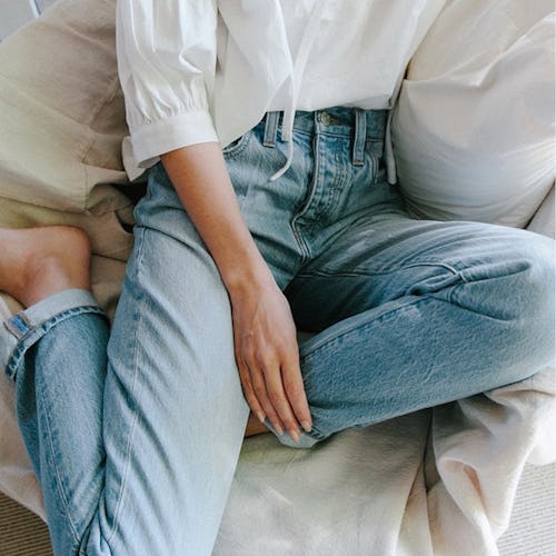 A model sitting and posing in blue denim jeans and a white shirt by J.Crew