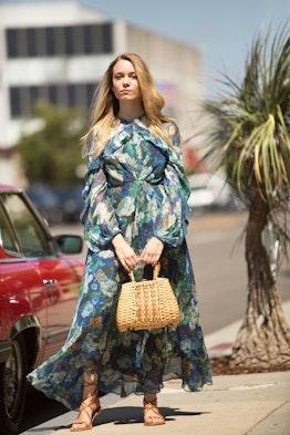 A blonde woman posing in a blue esplanade flute dress while holding a brown tote 