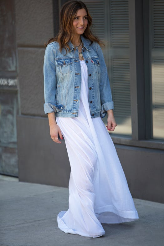 A brunette woman walking in a white dress and a trucker jacket
