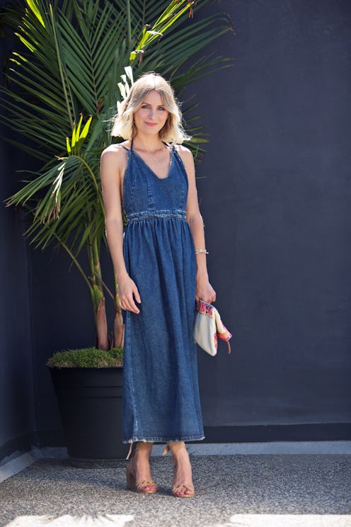 A blonde woman with a bob haircut posing next to a palm tree in a summer maxi denim dress
