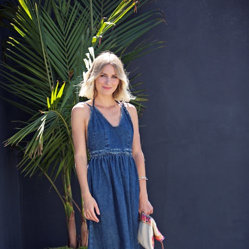 A blonde woman with a bob haircut posing next to a palm tree in a summer maxi denim dress