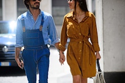 A woman in a suede dress holding hands with a man in a denim shirt and denim overalls